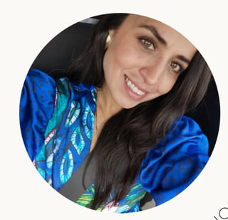 Woman with long dark hair smiling at camera, wearing bright blue jacket with colorful feather print design