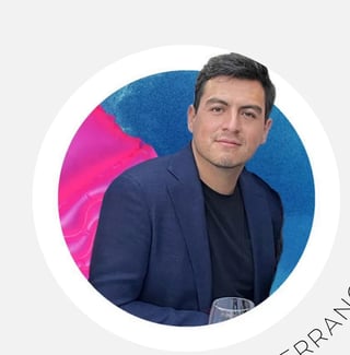 Professional headshot of a man in a dark blazer and black shirt against a blue and pink circular background
