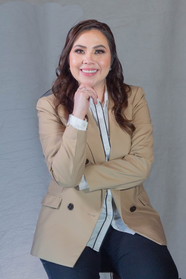 Professional headshot of a smiling woman with long dark wavy hair wearing a beige blazer over a white striped shirt