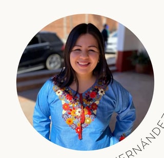 Woman in blue shirt with colorful embroidered neckline smiling at camera in circular portrait